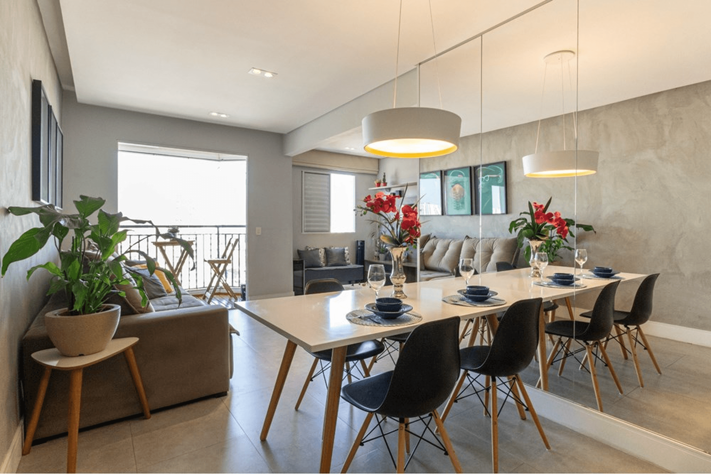 Sala de estar e jantar integrada com mesa de jantar, cadeiras pretas e parede revestida com espelho.